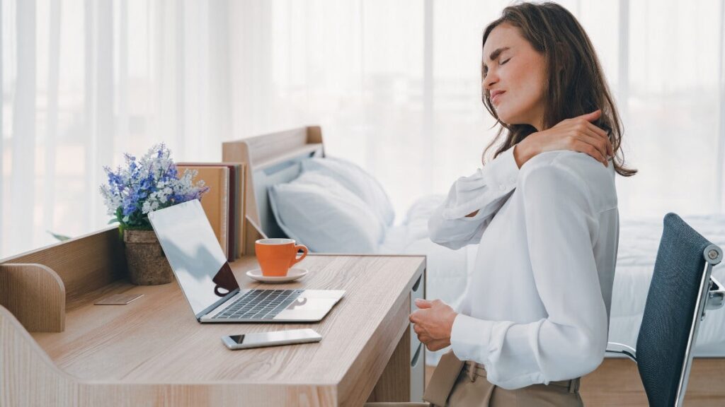Femme assise au bureau souffrant de douleurs cervicales, illustrant le besoin de remèdes maison