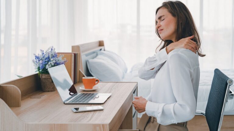Femme assise au bureau souffrant de douleurs cervicales, illustrant le besoin de remèdes maison