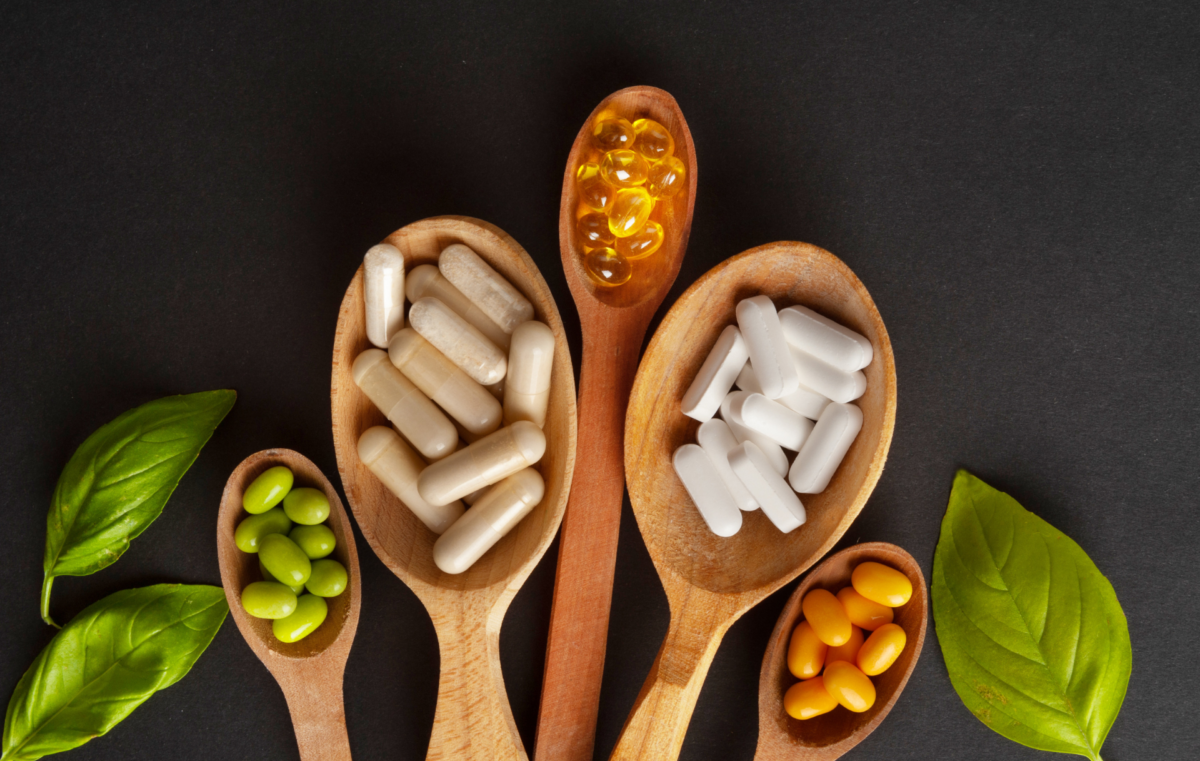 Différents compléments alimentaires en gélules et comprimés disposés sur une table à côté d'une étiquette de composition